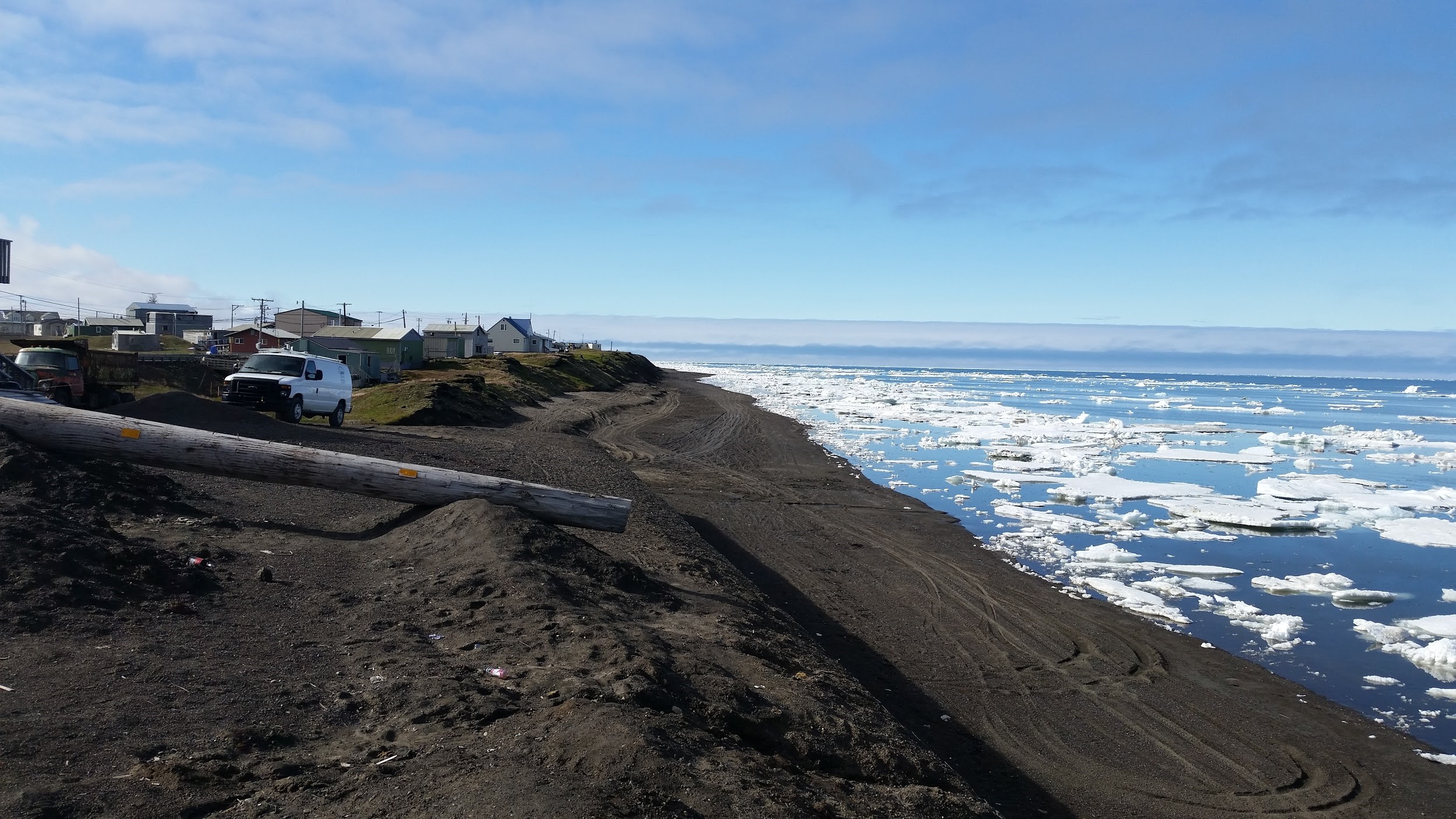 Ancient dwelling mounds (foreground) and modern homes alike are threatened by rising sea levels along Alaska’s North Slope. Image courtesy of Michael Brady/Rutgers. 