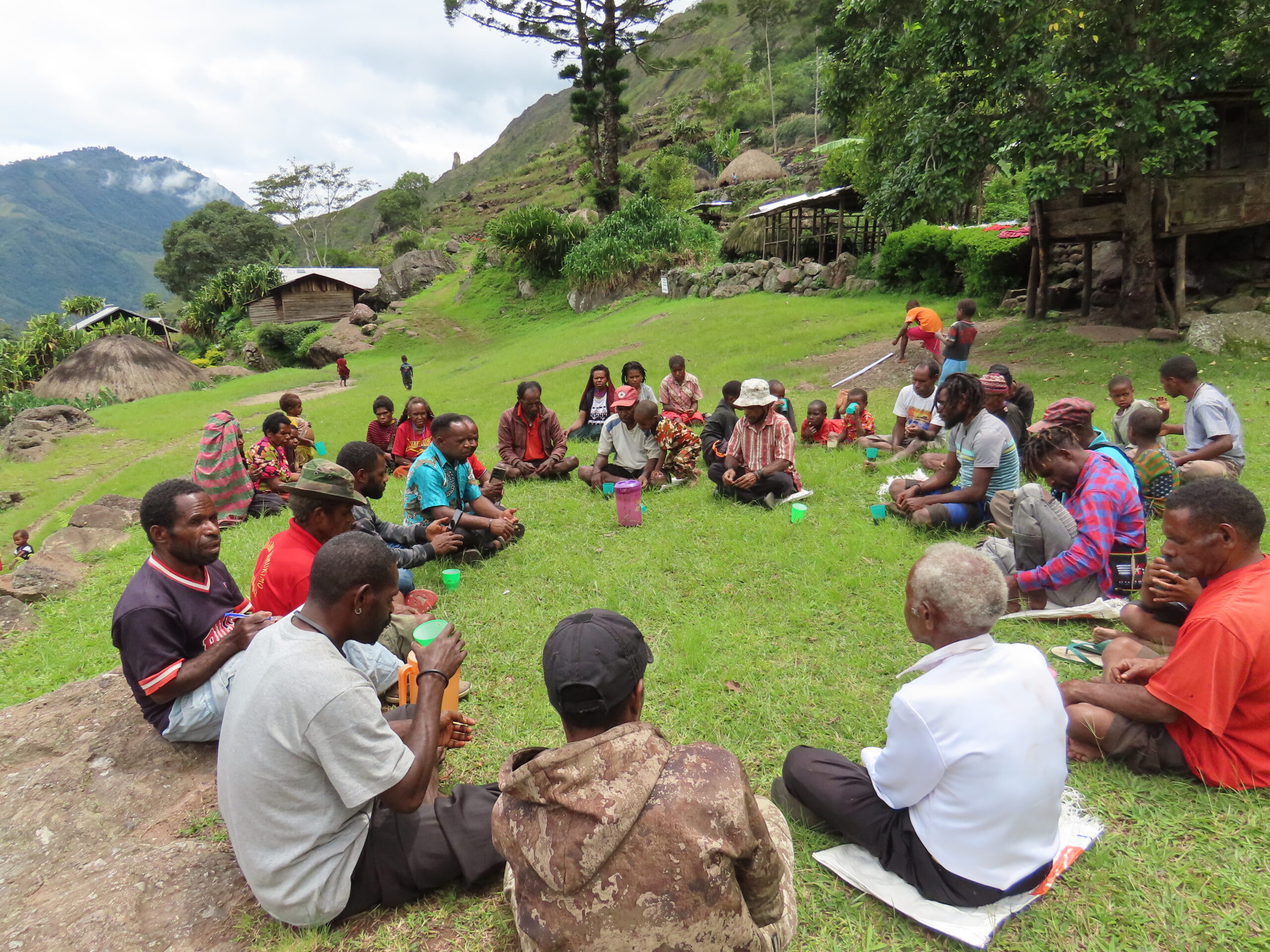 Community members in Papua sit in a circle in an open grassy area to discuss.