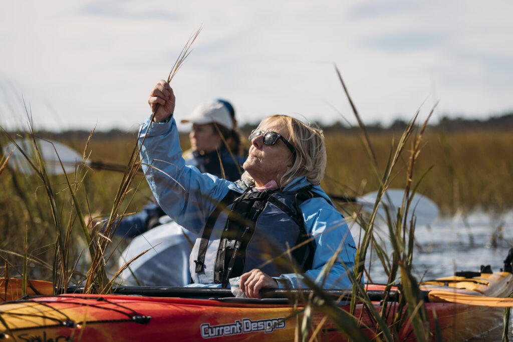 a woman in a kayak holds a plant up to examine