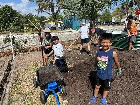 Students smile at the camera as they work on the community garden