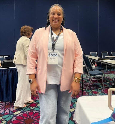 Photo of Camille standing and smiling at the camera wearing a light salmon colored cardigan